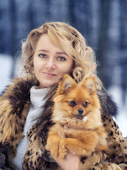 A beautiful young woman is walking with a dog through a snowy forest. Concept. Caring for pets. Spitz puppy. Winter.