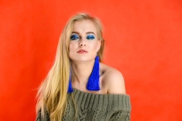 A woman shows different emotions. A pretty blonde model with long hair and excellent make-up is standing in front of the camera on a red background in a green jacket.