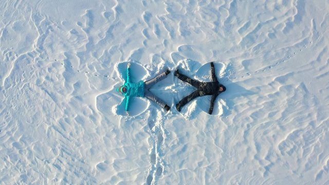 A family makes a figure of a snow angel in a clearing in the forest. Aerial photography of a girl and a boy lying on the snow.