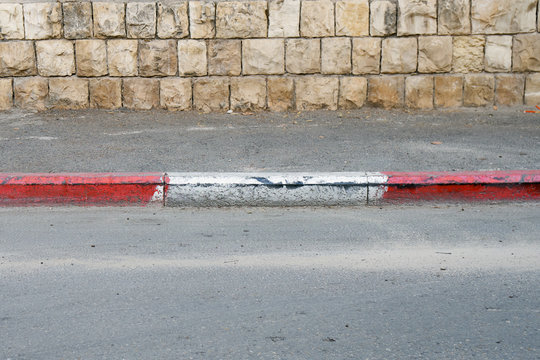 Red and white colored road curbstone indicating the prohibition of Parking on Israel street