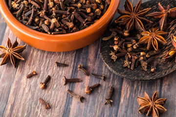 Top down view of a bowl of cloves surrounded by cloves and star anise.