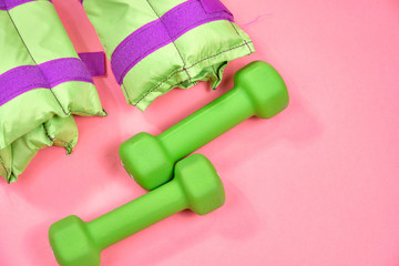 Fitness equipment, green dumbbells and weights on a pink background, space for text