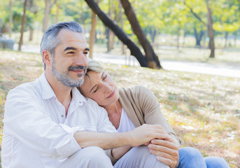 Senior couple was sitting on the lawn in the park hugs and smiles happily. concept of living after retirement