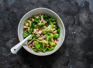 Warm salad with beans, baked chicken breast, romaine lettuce on a dark background, top view