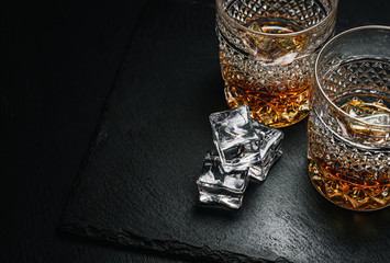two expensive glasses of whiskey with ice on a black stone tray