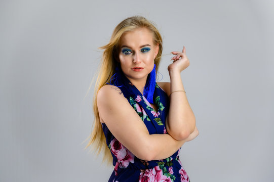 The model stands in different poses. Nice girl with fluttering hair and great make-up in front of the camera on a white background in a multi-colored dress.