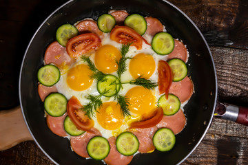 Top view. In the pan is a fried egg with sausage, tomatoes, cucumber and dill.