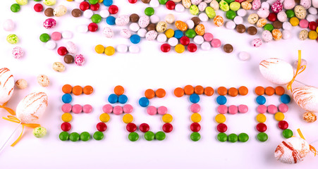 the word Easter is written in colorful bright round candies on the background of decorative eggs and candies