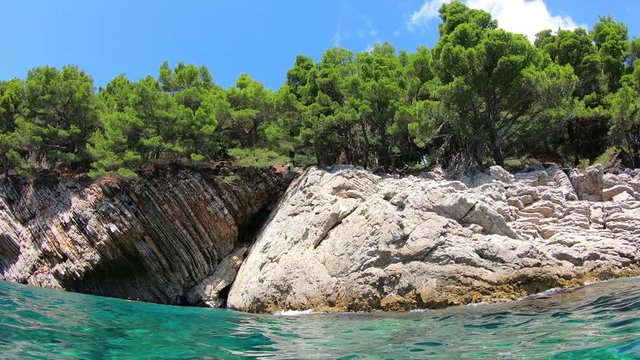 Layered cliffs and bright clear sea water, cave and sedimentary rocks rising from the bottom of the Adriatic sea in Petrovac, Montenegro