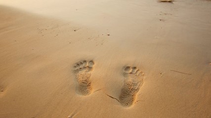 Human footprints on bare sand washes away by wave