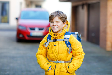 Little school kid boy of elementary class walking to school. Portrait of happy child on the street with traffic. Student with in yellow jacket and backpack in colorful winter clothes.