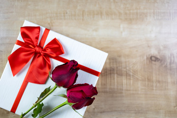 Two red flowers placed on a white gift box.