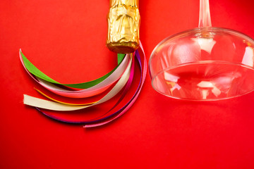 Champagne bottle neck in gold foil, colorful colored satin ribbons, with wine glass  on red...