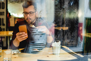 Young Man eating in restaurant and looking at mobile phone