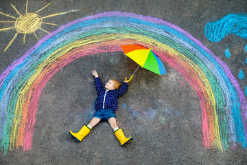 Happy little toddler girl in rubber boots with rainbow sun and clouds with rain painted with...