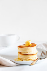 Fluffy Japan souffle pancakes, hotcakes with butter and maple syrup or honey sauces on light white background with copy space. Trendy asian food for breakfast. Vertical orientation