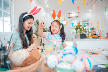 Attractive young woman with little cute girl are preparing for Easter celebration. Mom and daughter wearing bunny ears are having fun with Easter bunny while at home.