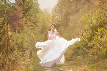Fototapeta na wymiar A beautiful bride is walking in nature, on a green lawn between branches and trees. Photography and concept