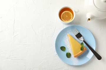 Plate with lemon tart slice, teapot and cup of tea on white background, top view