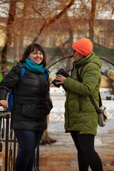 Two girls take pictures and walk in a city park on a sunny day in early spring. A girl photographer takes a picture of a model and then watches the photos together on the camera.