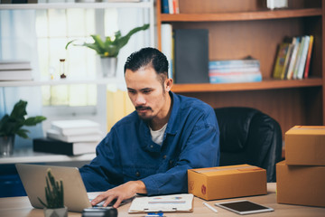 Fototapeta premium Small business owner packing in the box at workplace. Cropped shot of man preparing a parcel for delivery at online selling business office.