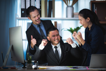 Three excited employees reading good news online in a computer sitting in a desktop at office