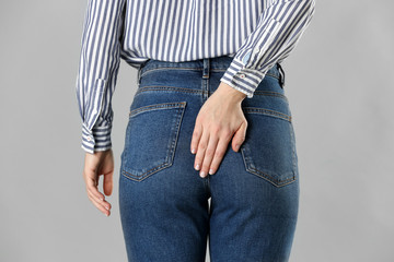 Woman suffering from hemorrhoid on light grey background, closeup