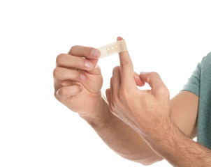 Man putting sticking plaster onto finger on white background, closeup
