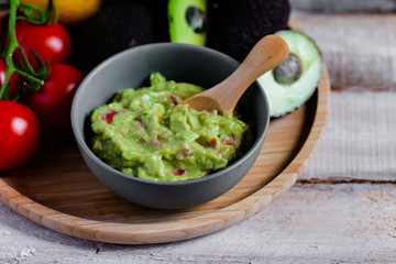 Tasty and healthy mexican snack: avocado guacamole. Homemade, served on a wooden rustic table with raw ingredients. Delicious and low calorie meal to share with friens. Close up, macro