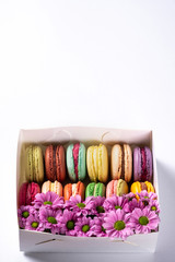 Colorful macaroons with flowers in gift box on white background. Valentines Day (14 February), Mother's day, Birthday or Woman's day (8 March) concept. French almond macaron cookies. Copy space