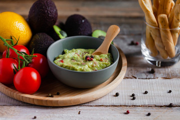 Tasty and healthy mexican snack: avocado guacamole. Homemade, served with bread stick with herbs on a wooden rustic table. Delicious and low calorie meal to share for the company. Copy space for text