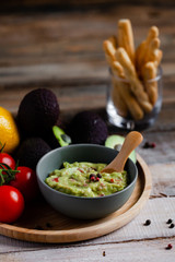Tasty and healthy mexican snack: avocado guacamole. Homemade, served with bread stick with herbs on a wooden rustic table. Delicious and low calorie meal to share for the company. Close up, macro