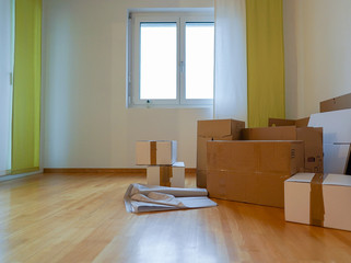 view of moving boxes and materials in an empty living room with wooden floor and white walls