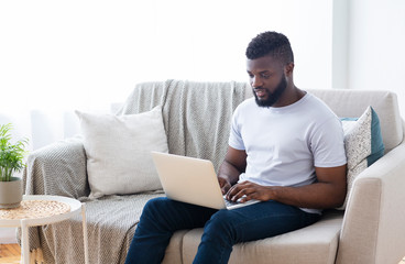 Young african man working on laptop online at home