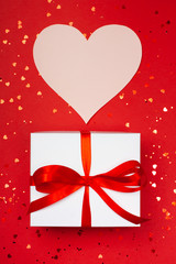 A gift with paper for notes in the shape of a heart on a red background. Surprise your loved one. The concept of the St. Valentine's day, birthday and other holidays. Flat lay