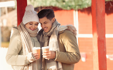 Happy couple in warm clothes with drinks at winter fair. Christmas season