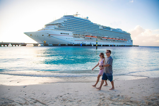 Middle aged couple enjoying a Caribbean Cruise vacation together. Candid photo of a couple holding hands and walking together on a beach with a Cruise ship in the background