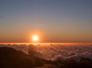 Beautiful red sunset above white clouds cover with sun rays and asphalt road at mountains at La Palma, Canary Island, Spain
