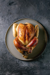 Whole baked chicken poultry on ceramic plate over black concrete background. Flat lay, space. Dinner menu