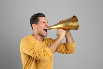 Handsome man with megaphone on grey background