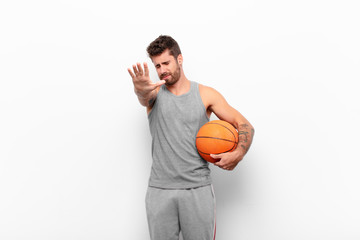 young handsome man covering face with hand and putting other hand up front to stop camera, refusing...