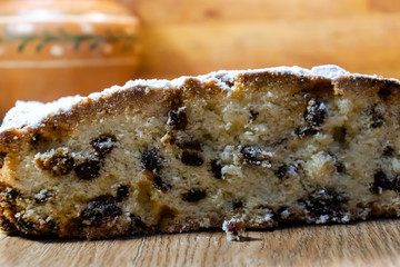 Tasty, delicious pie with raisins, sprinkled with icing sugar, cut on a wooden table. Cupcakes for holidays, dough products. With clay vintage pot in the background