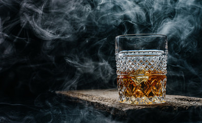Glas Whisky mit Eis auf einem Holztisch, umgeben von Rauch