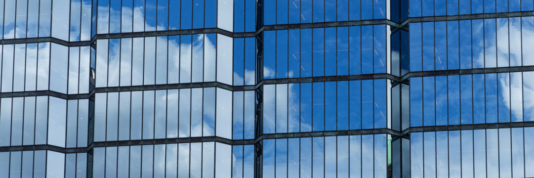 Panoramic image. Windows of a skyscraper with reflection of blue sky and white clouds
