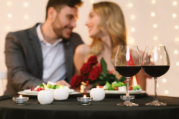 Affectionate couple dating in restaurant, glasses with red wine in foreground