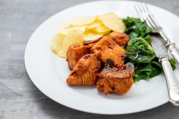 fried meat with potato chips and greens on white plate on ceramic background