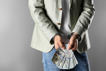Man in handcuffs holding bribe money on grey background, closeup - Powered by Adobe