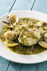 Hake fish and clams with green sauce on blue wooden table.Close up