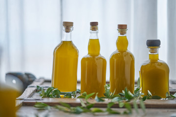 detail of four bottles filled with a yellow liquid that looks like oil sorted on a wooden furniture in front of a white curtain in a kitchen cooking book gourmet