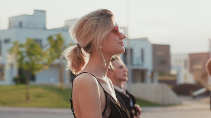 Profile of attractive blonde girl sitting among audience on seats outdoors. Close-up pretty business lady making bids for property raising hand showing paddle. Modern auction.